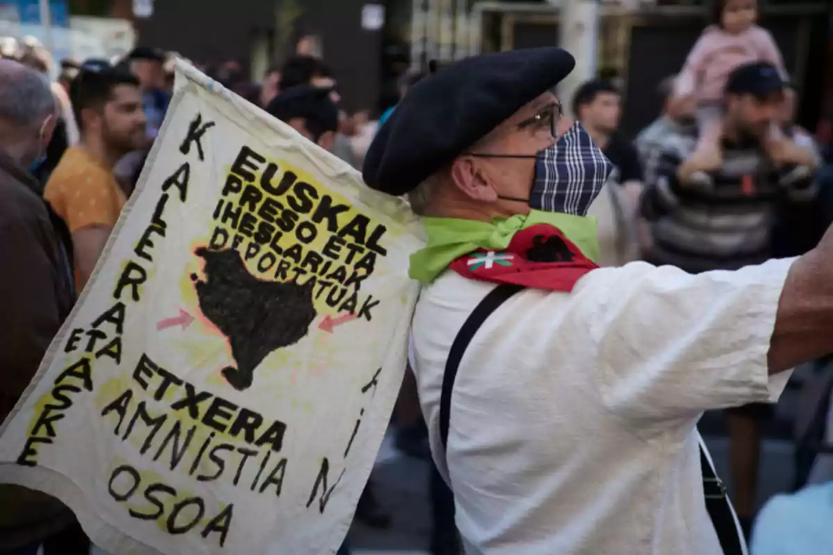 Hombre con boina y mascarilla sostiene una pancarta en una manifestación con mensajes en euskera pidiendo amnistía y libertad para presos Hombre con boina y mascarilla sostiene una pancarta en una manifestación con mensajes en euskera pidiendo amnistía y libertad para presos