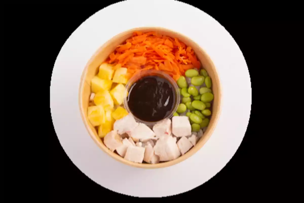 Ensalada en bowl con pollo en cubos, zanahoria rallada, edamames, piña y salsa en el centro