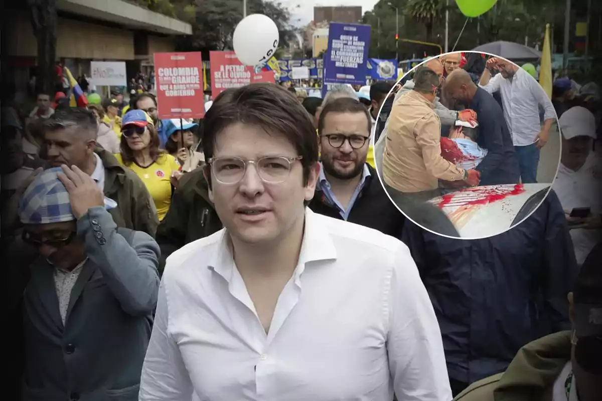 Un hombre con gafas y camisa blanca camina al frente de una manifestación con personas sosteniendo pancartas y globos, en la esquina superior derecha hay un recuadro que muestra a varias personas auxiliando a alguien herido con sangre visible sobre una superficie.
