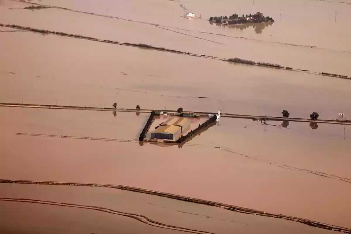 Vista aérea de una zona inundada donde se observa un edificio rodeado de agua y caminos parcialmente sumergidos.