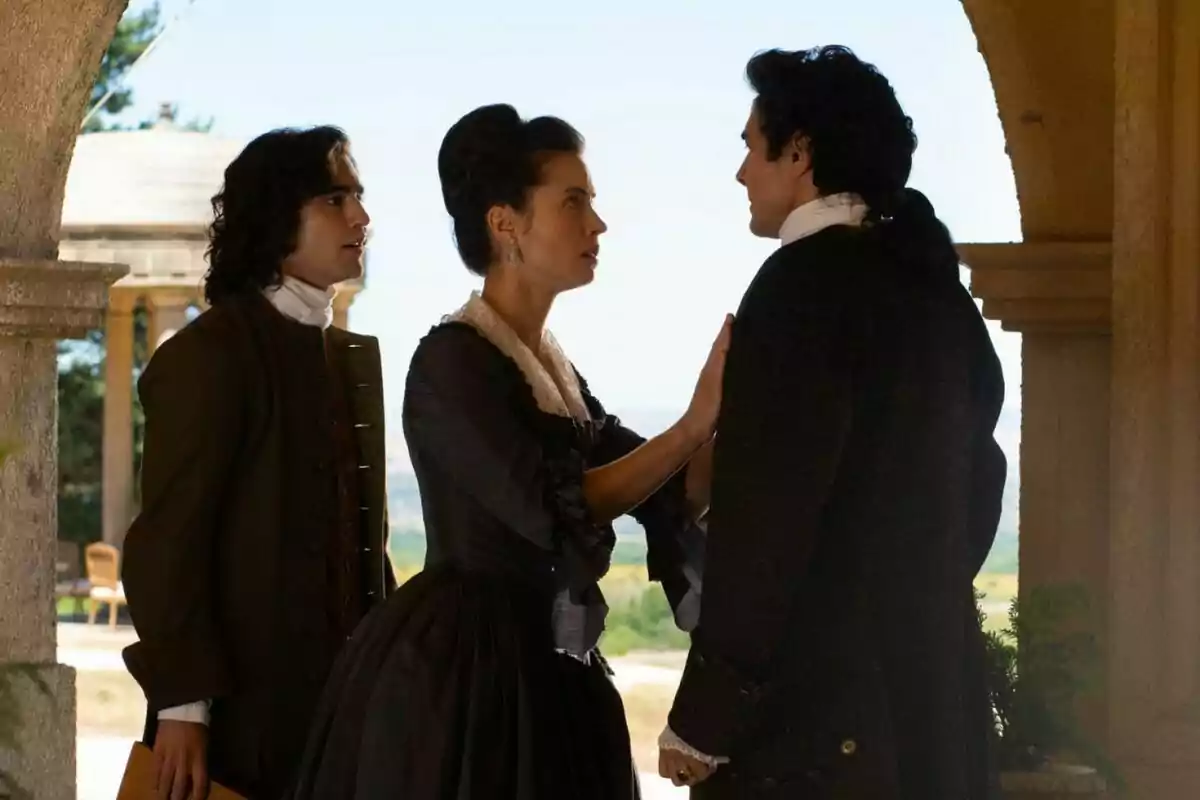 Alejo, Mercedes and José Luis dressed in period clothing are having a serious conversation under a stone arch in an outdoor setting. Capture from 'Valle Salvaje'