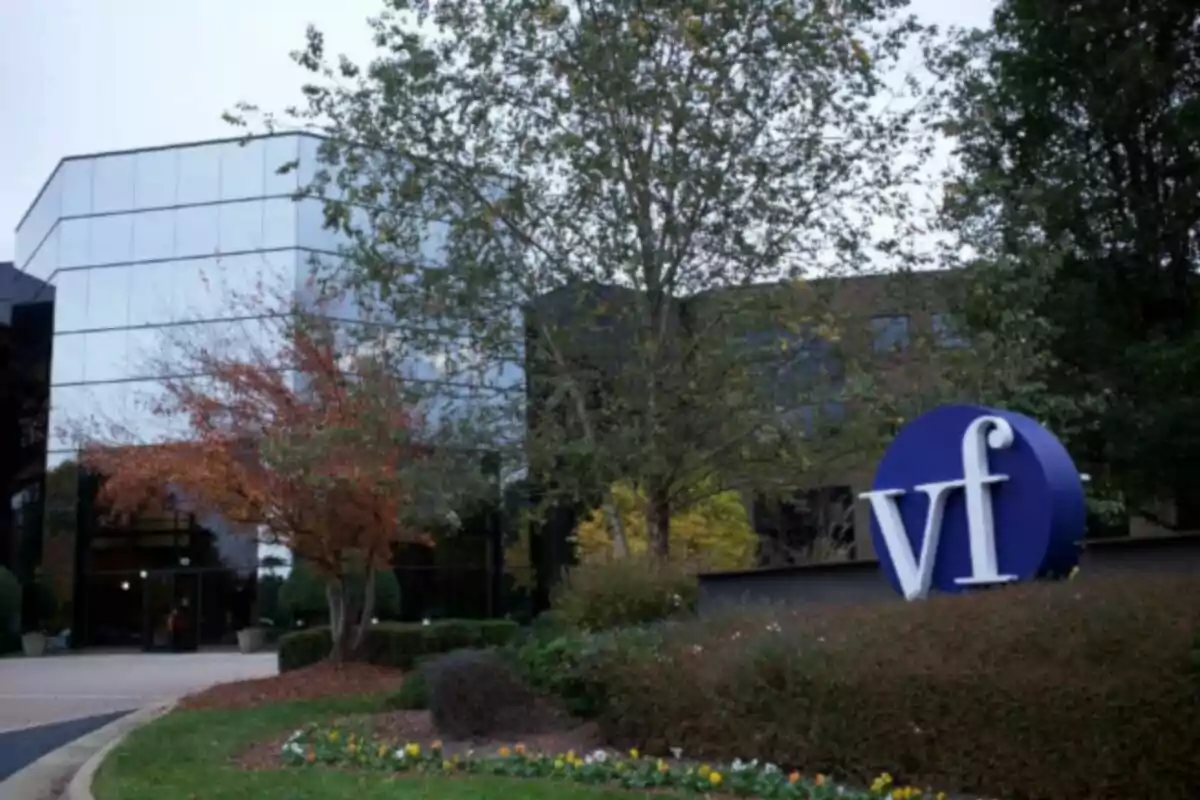 Modern building with a glass facade surrounded by trees and shrubs with a blue sign that has the letters Modern building with a glass facade surrounded by trees and shrubs with a blue sign that has the letters