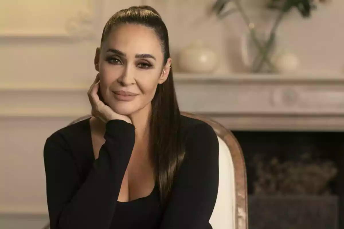 Vicky Martín Berrocal con cabello largo y oscuro sentada en una silla con la mano apoyada en el rostro en un ambiente interior elegante en Las Berrocal. Vicky Martín Berrocal con cabello largo y oscuro sentada en una silla con la mano apoyada en el rostro en un ambiente interior elegante en Las Berrocal.