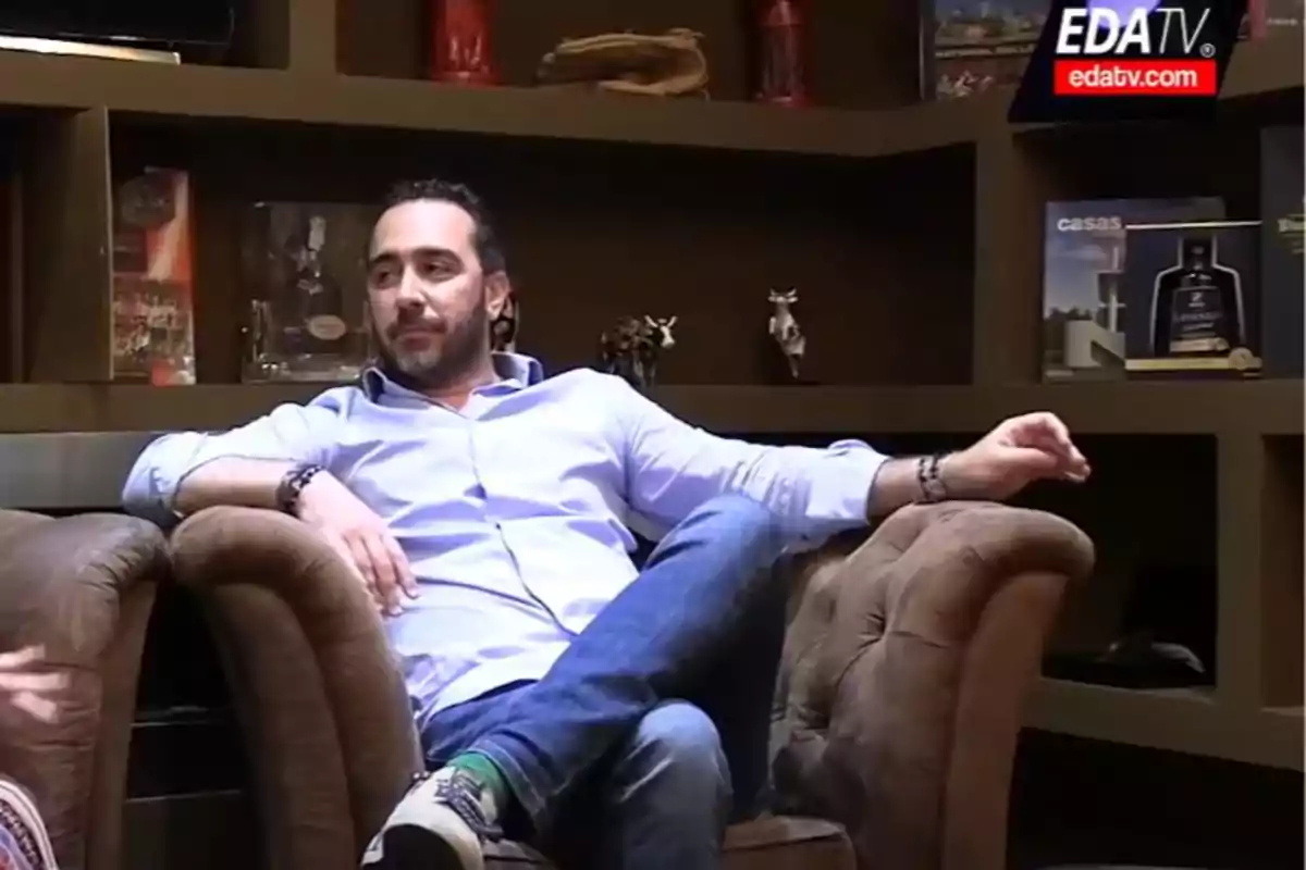 Man sitting in a brown armchair in a cozy environment with bookshelves in the background.