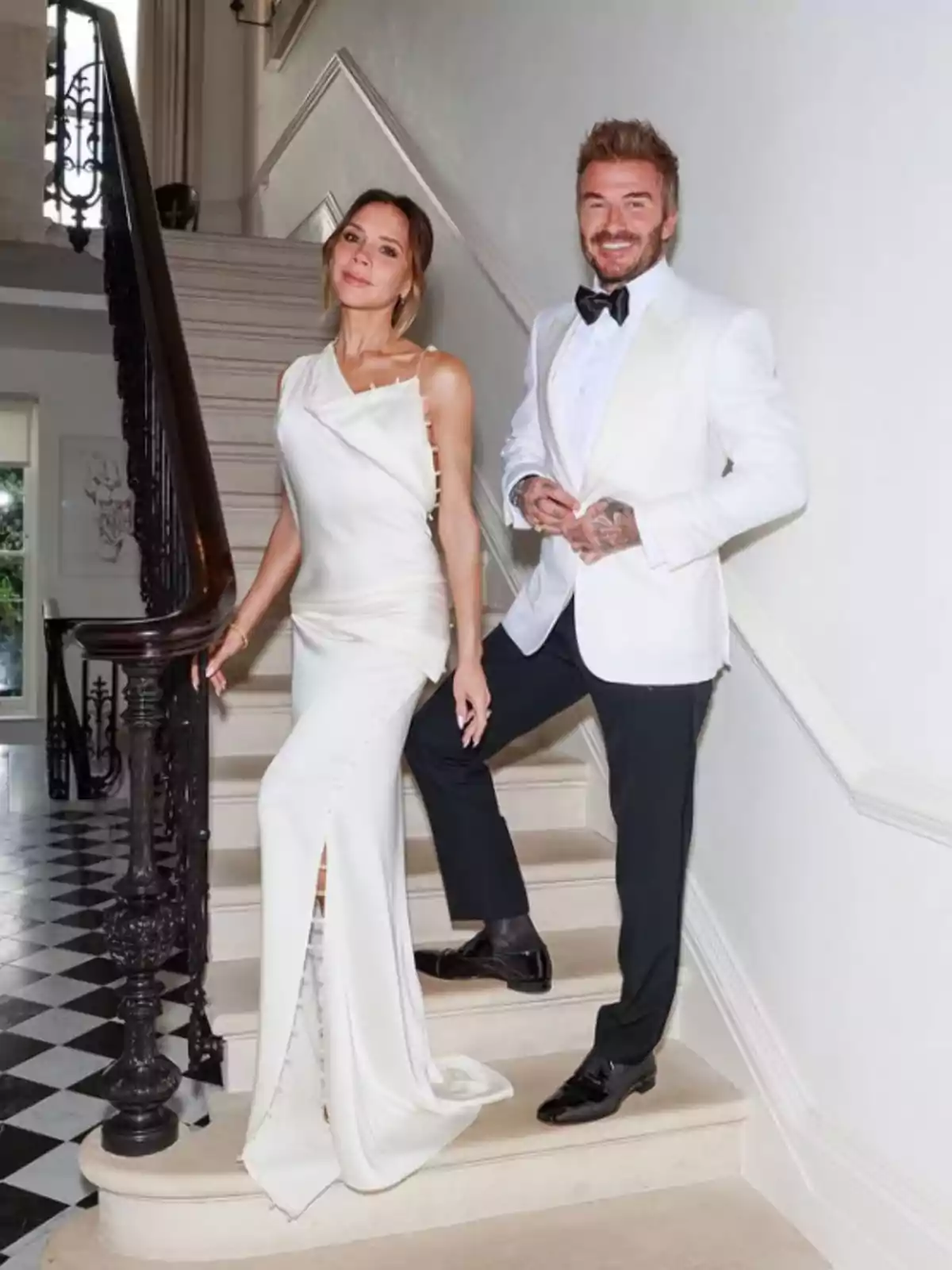 Una pareja elegantemente vestida posa en una escalera dentro de una casa, ambos llevan ropa formal en tonos blancos y negros Una pareja elegantemente vestida posa en una escalera dentro de una casa, ambos llevan ropa formal en tonos blancos y negros