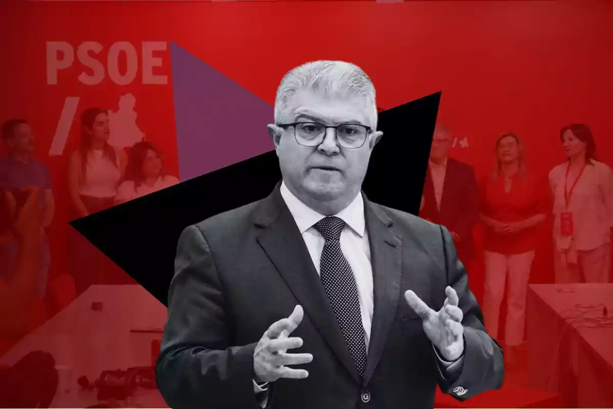 Un hombre con traje y corbata, de cabello canoso y gafas, gesticulando con las manos frente a un fondo rojo con el logotipo del PSOE y varias personas en segundo plano.