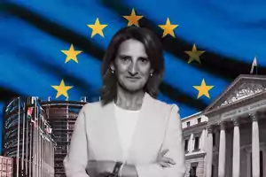 Una mujer de pie con los brazos cruzados frente a un fondo de la bandera de la Unión Europea y edificios gubernamentales.