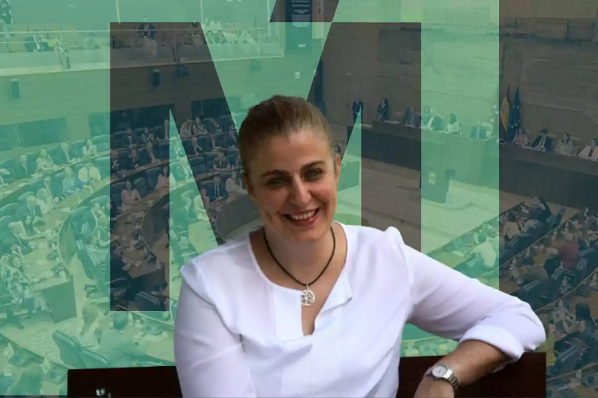 Una mujer sonriente con una camisa blanca y un collar, con un fondo de una asamblea legislativa y letras grandes en color verde.