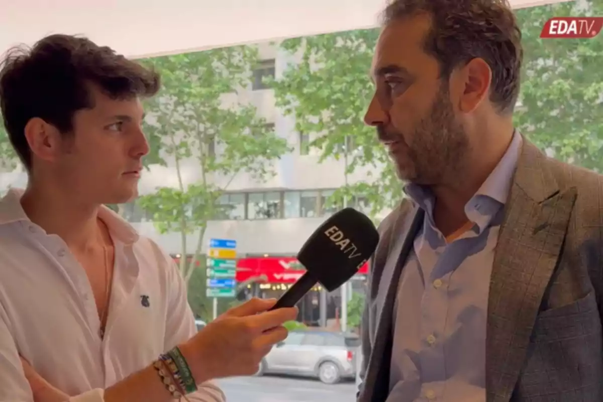 Dos hombres conversan durante una entrevista en la calle mientras uno sostiene un micrófono con el logo de EDA TV