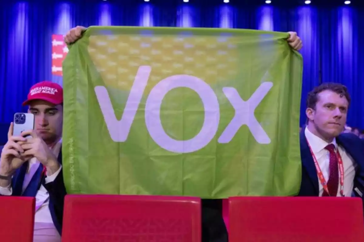 Dos asistentes al VIVA Vox 24 sacan una bandera de Vox