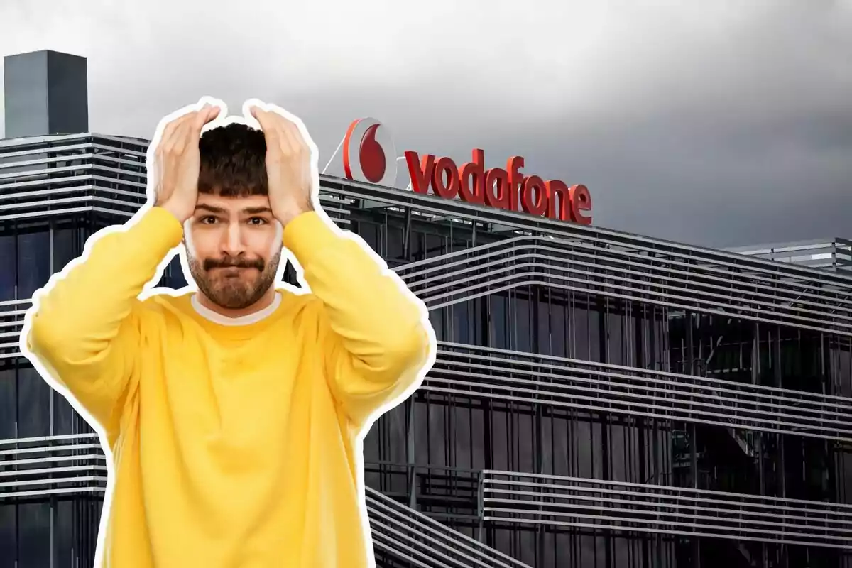 Un hombre con suéter amarillo se muestra preocupado frente a un edificio de oficinas con el logo de Vodafone.