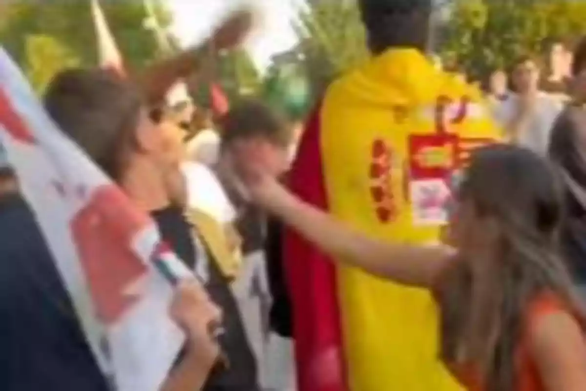 Una mujer extiende el brazo hacia un hombre en una manifestación donde varias personas portan banderas y una persona lleva una bandera de España sobre los hombros Una mujer extiende el brazo hacia un hombre en una manifestación donde varias personas portan banderas y una persona lleva una bandera de España sobre los hombros
