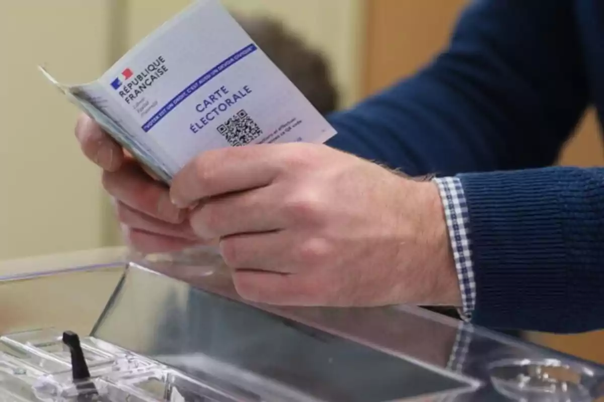 Persona sosteniendo una tarjeta electoral francesa sobre una urna de votación.