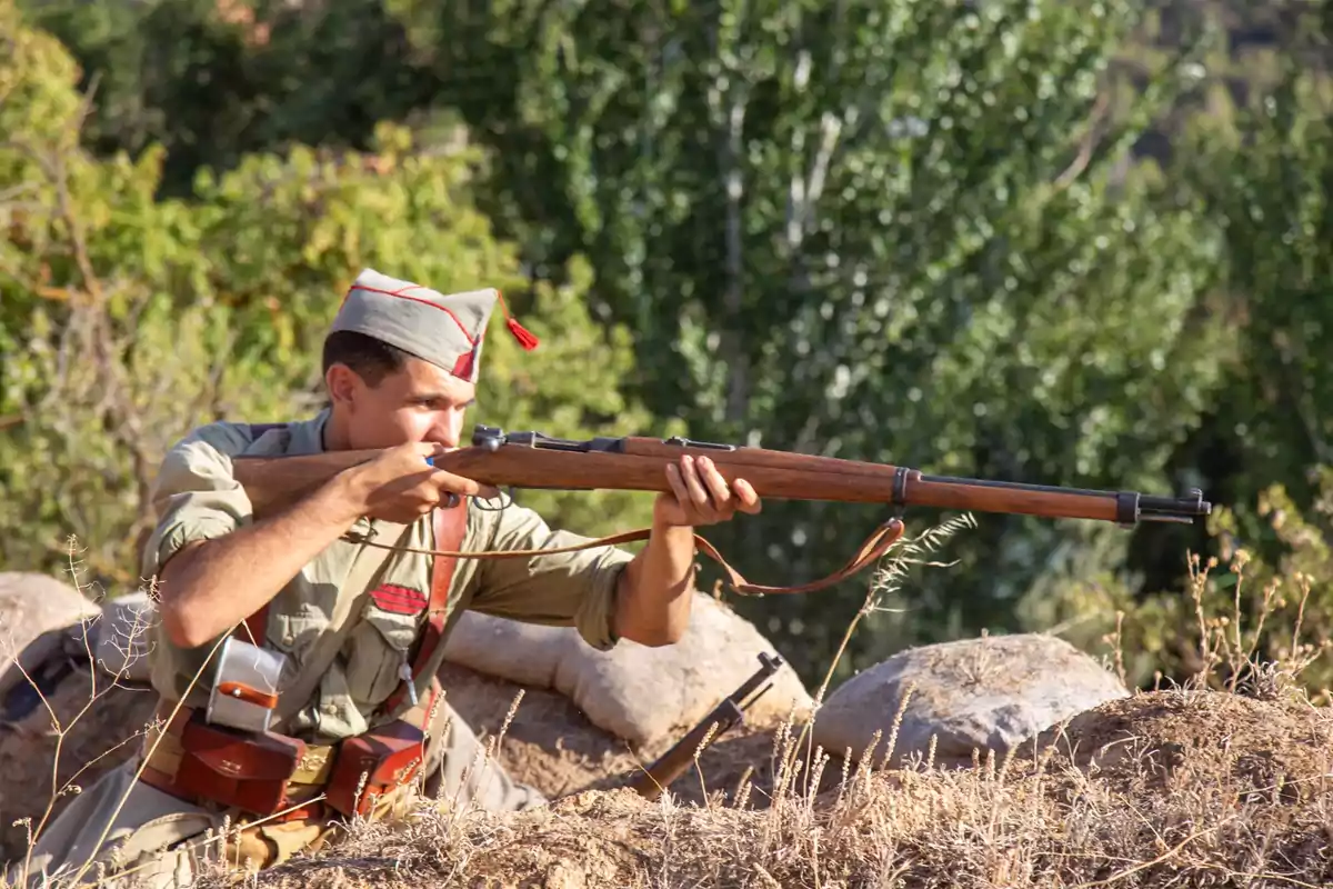 Un soldado apuntando con un rifle en un entorno natural.