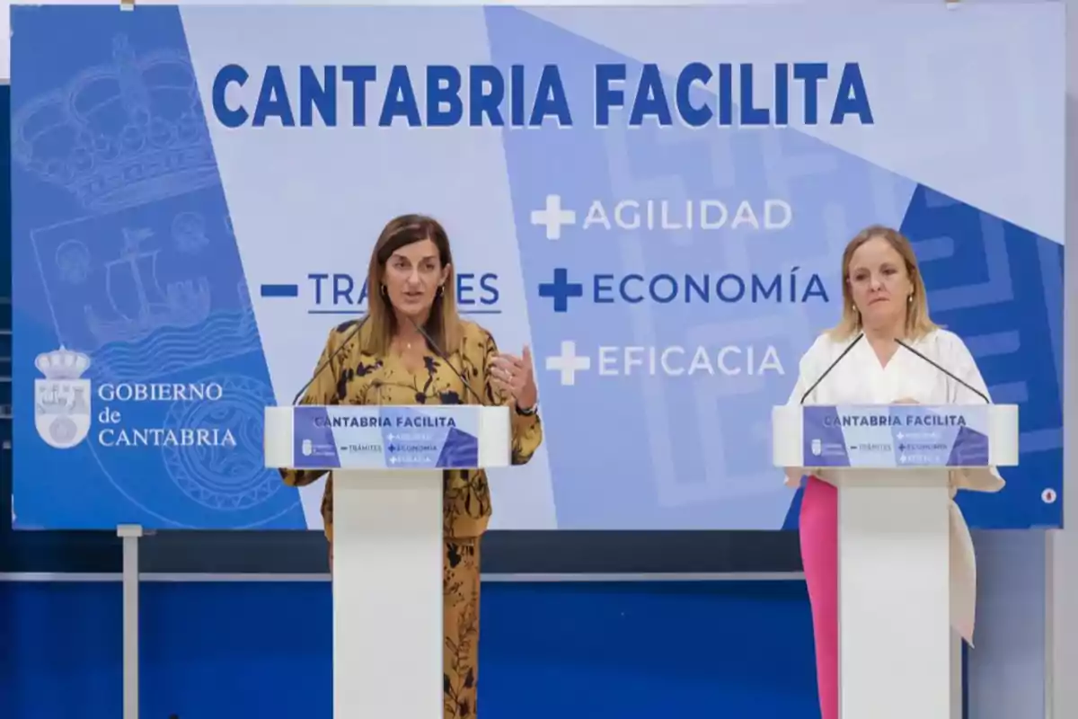 Dos mujeres en un podio durante una conferencia de prensa del Gobierno de Cantabria, con un cartel de fondo que dice "Cantabria Facilita" y menciona "Trámites", "Agilidad", "Economía" y "Eficacia".