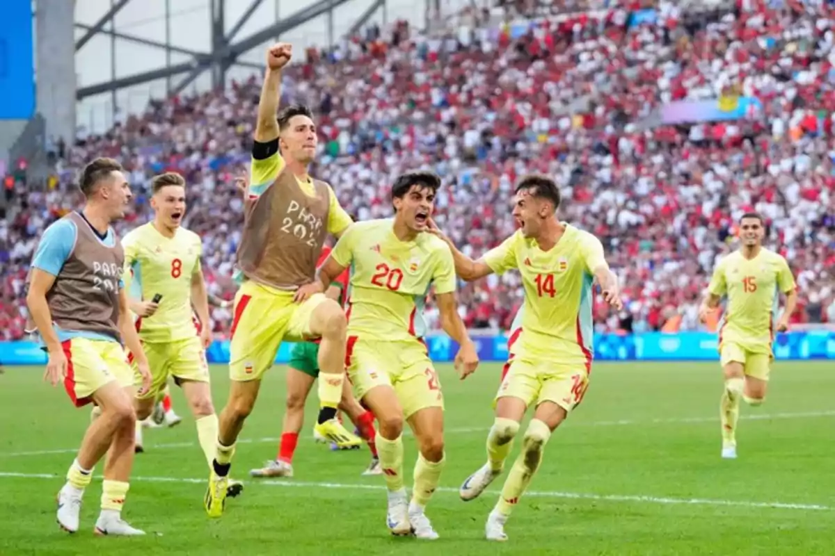 Jugadores de fútbol celebrando un gol en un estadio lleno de aficionados.