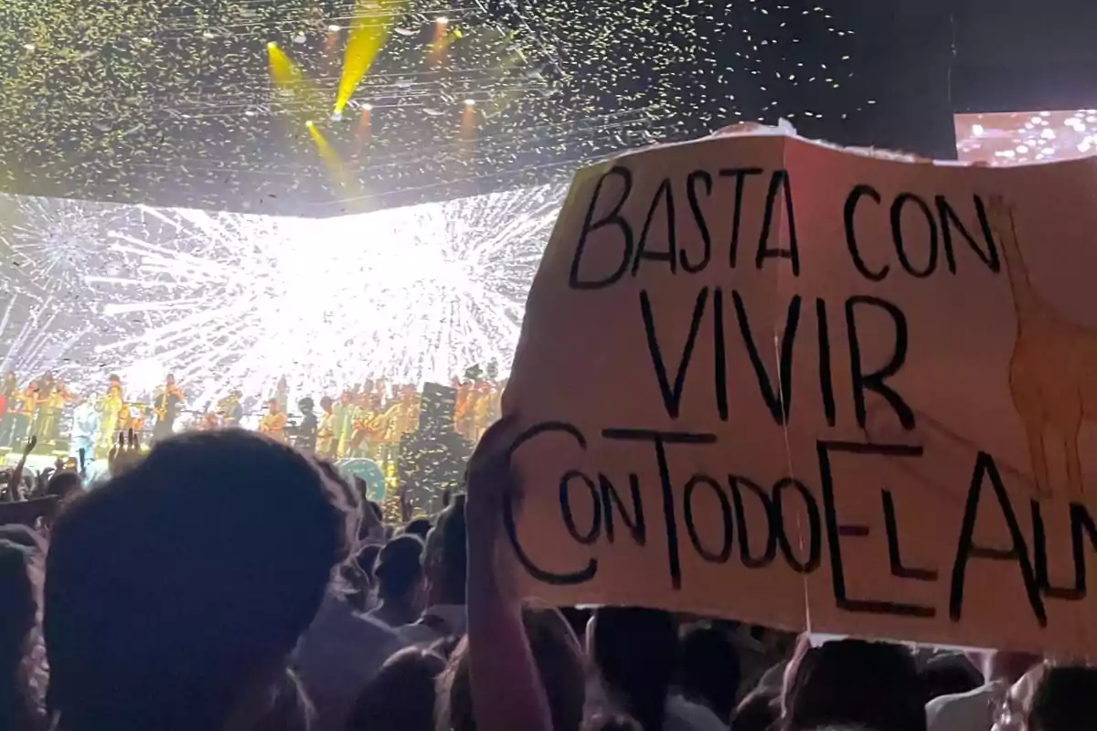 Una multitud en un concierto con un cartel que dice "Basta con vivir con todo el alma" y fuegos artificiales en el escenario.