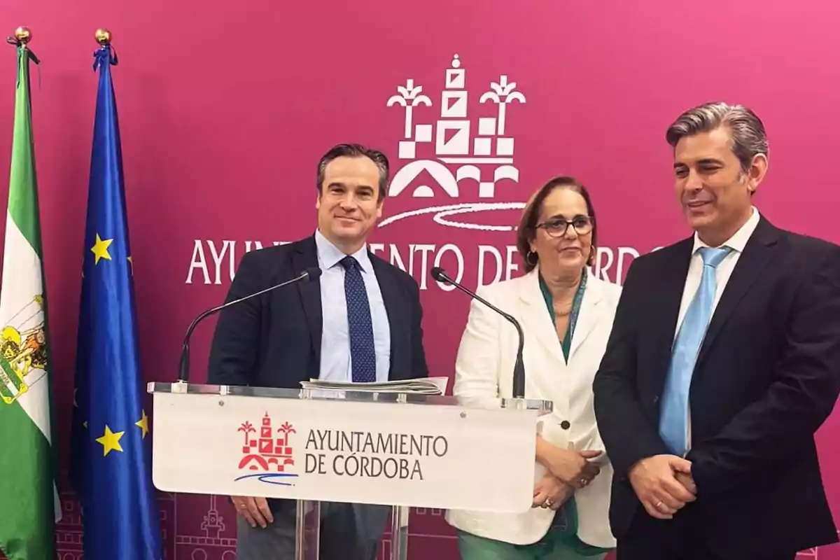 Tres personas posan frente a un podio con el logotipo del Ayuntamiento de Córdoba, acompañadas de las banderas de Andalucía y la Unión Europea.