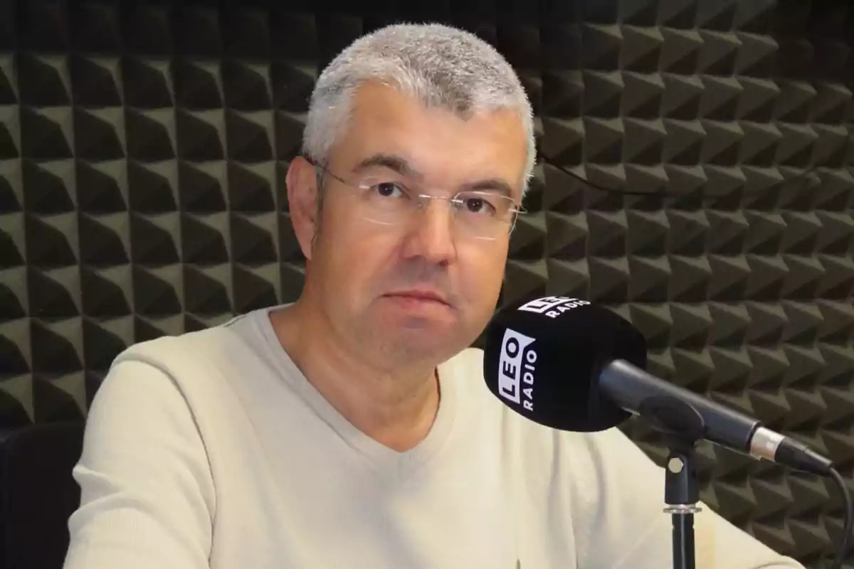 Hombre con gafas y cabello canoso frente a un micrófono en un estudio de radio.