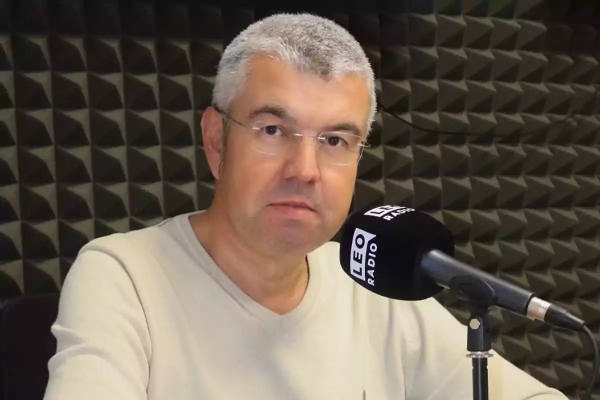 Hombre con cabello canoso y gafas frente a un micrófono en un estudio de radio.