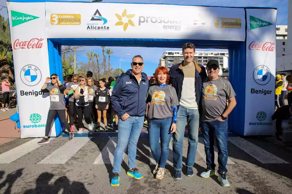 A group of people poses in front of an inflatable arch at the starting line of a race, with several sponsor logos visible on the arch.