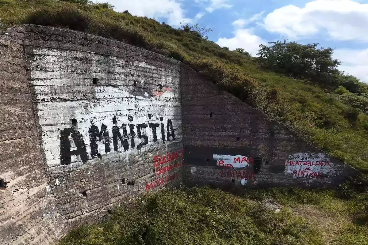 Un muro de concreto en una colina con grafitis en letras grandes que dicen amnistía y otros mensajes en rojo y negro Un muro de concreto en una colina con grafitis en letras grandes que dicen amnistía y otros mensajes en rojo y negro