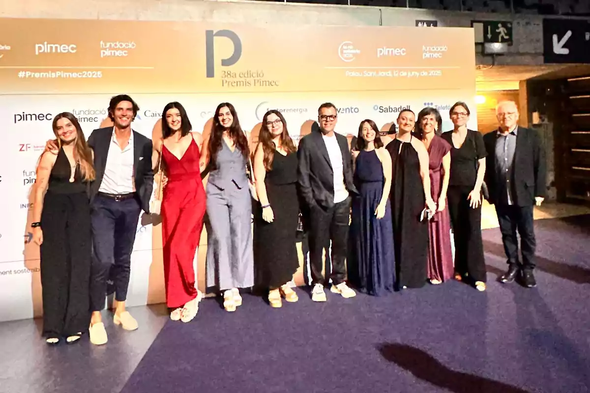 Un grupo de personas elegantemente vestidas posa sonriente frente a un fondo de un evento de premiación empresarial.