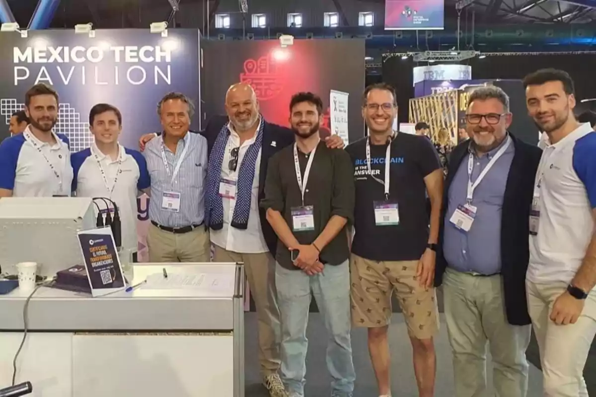 Ocho hombres posan sonrientes frente a un stand que dice Mexico Tech Pavilion en un evento tecnológico