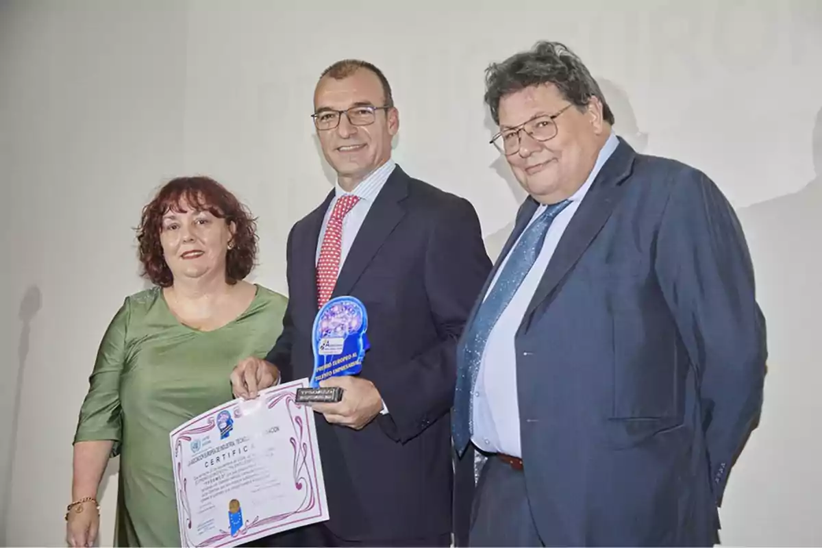 Tres personas posan juntas mientras una de ellas sostiene un certificado y un trofeo.