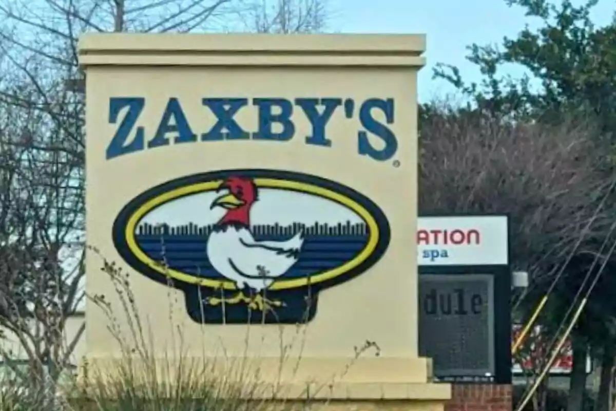 Zaxby's sign with a drawing of a chicken in the center surrounded by trees and vegetation. Zaxby's sign with a drawing of a chicken in the center surrounded by trees and vegetation.