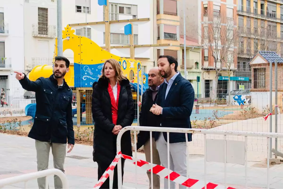 A group of people is watching a playground under construction behind a safety fence.